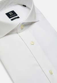 Bela, s dolgimi rokavi srajca z klasičnim ovratnikom, rumenimi gumbi in gladko teksturo tkanine. Oznaka blagovne znamke vidna znotraj ovratnika.