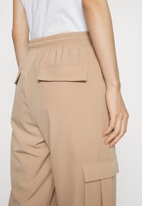 Beige cargo nohavice s elastickým pásom, dvoma zadnými vreckami a hladkým povrchom. Majú voľný strih a dodatočné bočné vrecká ako akcenty.