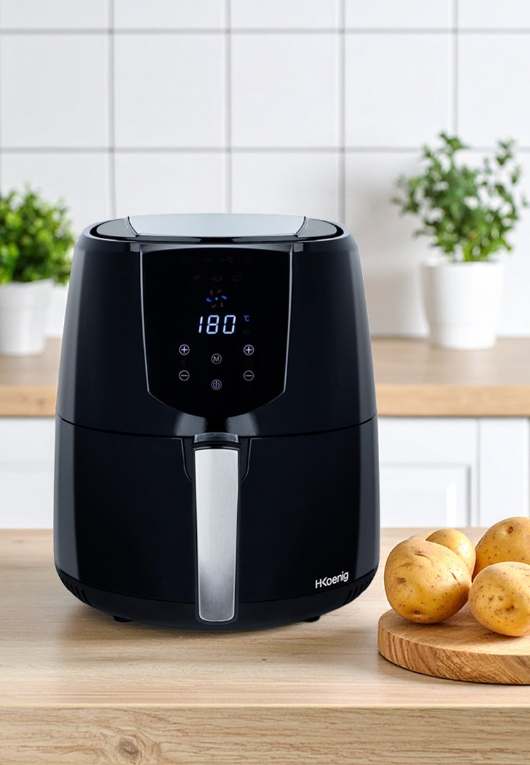 Friteuse à air noire avec un affichage numérique, poignée argentée, forme arrondie et extérieur élégant. Pommes de terre sur une planche à découper en bois à proximité.