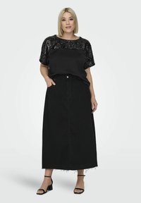 Czarna koszula z cekinami w połączeniu z czarną maksi spódnicą dżinsową. Spódnica ma postrzępiony brzeg i kieszenie z przodu. Modelka nosi czarne sandały na obcasie.