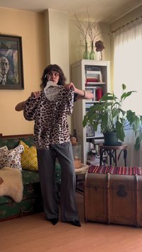 Blusa de estampado animal com mangas curtas e bufantes, predominantemente bege com manchas castanhas escuras. Tecido leve, exibida num cabide, situada numa sala acolhedora.