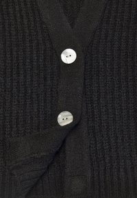 Černý žebrovaný cardigan s hlubokým výstřihem do V, vybavený třemi kulatými, světle zabarvenými knoflíky a jemným, texturovaným pleteným designem.