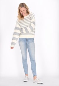 Gestreifter Pullover in Creme und Grau, mit lockerem Schnitt und weiten Ärmeln, kombiniert mit hellblauen Skinny Jeans und weißen Sneakers.
