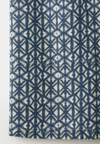 Tissu à motif géométrique bleu et blanc avec des figures répétées en forme d'étoile et des lignes verticales.