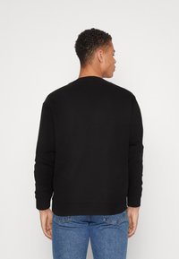 Czarna bluza z okrągłym dekoltem i długimi rękawami, wykonana z miękkiego materiału. Noszona z niebieskimi dżinsami, prezentująca prosty widok z tyłu.