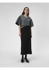 Graues, kurzärmliges Oberteil mit Puffärmeln, kombiniert mit einem schwarzen, figurbetonten Midirock. Das Outfit wird durch spitze schwarze Absätze ergänzt.