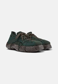 Dark green athletic shoes with a textured upper and chunky, speckled soles, featuring intricate lacing across the front.
