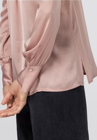 Långärmad blus i mjuk rosa satin, med veckade ärmar, knäppning i ärmsluten och sidsprund i fållen för extra detaljer.