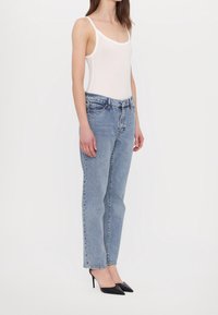 Biały bodysuit bez rękawów, jasnoniebieskie dżinsy z wysokim stanem i czarne, szpilki z ostrym noskiem. Dopasowany krój, casualowy design z gładką teksturą.