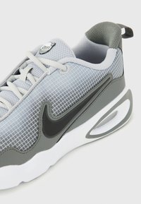 Sapatilha com um upper em malha cinza apresentando um padrão de grelha, logotipo Swoosh preto, gola acolchoada e uma entressola branca com unidade de ar visível.