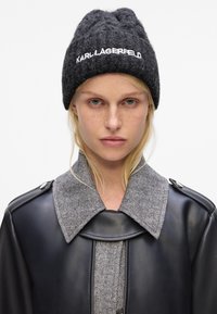 Gorro de lana de carbón con el logo "KARL LAGERFELD", combinado con una chaqueta de cuero negra que presenta un cuello de espiga gris y un tejido texturizado.