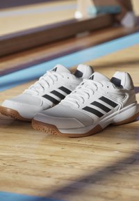 Baskets blanches de sport avec des rayures noires, tige en mesh, semelle en caoutchouc, détails texturés et col rembourré. Semelle extérieure en caoutchouc gomme pour une traction optimale.