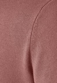 Różowy sweter o gładkiej, dzianinowej strukturze i subtelnym przeszyciu wzdłuż szwów. Materiał wydaje się miękki i lekki.