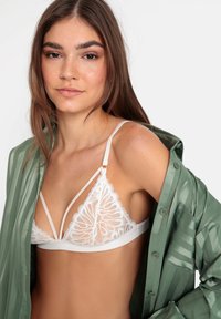 Hvit blonde bralette med blomsterdesign og gjennomskinnelige elementer. Kombinert med en grønn, svakt gjennomsiktig skjorte med knapper.