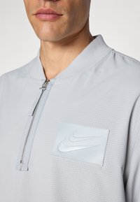 Light gray Nike pullover with a half-zip neck, featuring a textured fabric, perforations, and a raised logo patch on the chest.