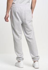 Lichtgrijze sweatpants met een elastische tailleband, iets taps toelopende benen en ribgebreide boorden. Bevat een enkele achterzak en heeft een zachte textuur.