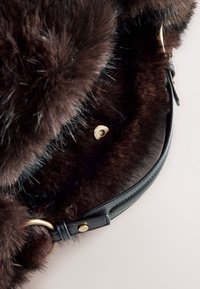Doublure en fourrure marron foncé avec sangle en cuir noire et détail d'un bouton doré sur le bord incurvé d’un accessoire ou vêtement.
