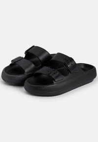 Sorte sandaler med to justerbare stropper, laget av glatt plastmateriale, med en strukturert såle for bedre grep.