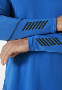 Langsleeve sportshirt van blauwe stof met een gestructureerde weving. Bevat zwarte diagonale streepaccenten bij de polsen, met platte naden.