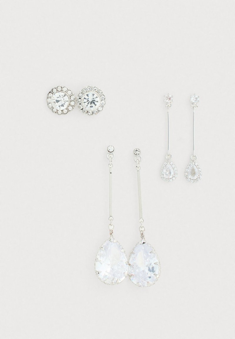 Quatre paires de boucles d'oreilles : deux paires de clous d'oreilles circulaires avec des strass clairs, et deux paires de boucles d'oreilles pendantes avec des cristaux en forme de poire en métal argenté.