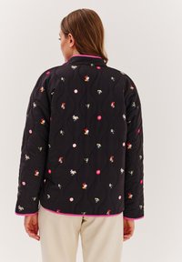 Čierna prešívanej bunda s farebnými vyšívanými postavami a kvetinovými motívmi; má ružový lem okolo goliera a manžiet.