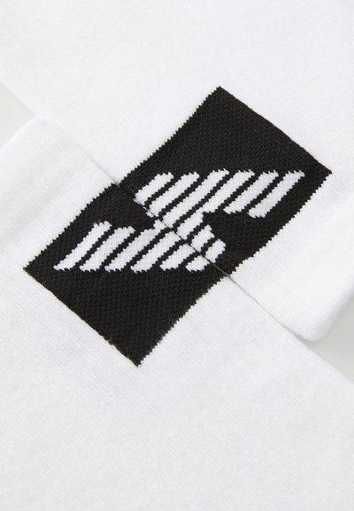Balti sporta zeķes ar melnu logo uzlīmi, kas iezīmē horizontālas un diognālas baltas svītras. Materiāls izskatās gluds un mīksts.
