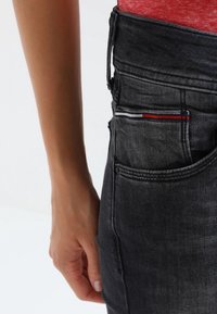 Jeans de mezclilla negros deslavados con una cintura ajustada, que presentan un detalle de bolsillo a rayas multicolores y una textura suave.