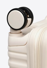 Walizka na kółkach w matowym beżowym kolorze o teksturowanym wykończeniu, z cylindrycznym czarnym wzorem kółek i bocznym zamkiem błyskawicznym.