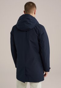 Parka impermeable de color azul marino con capucha, que cuenta con una ventilación trasera, textura suave y un diseño minimalista. Puños ajustables con snaps.