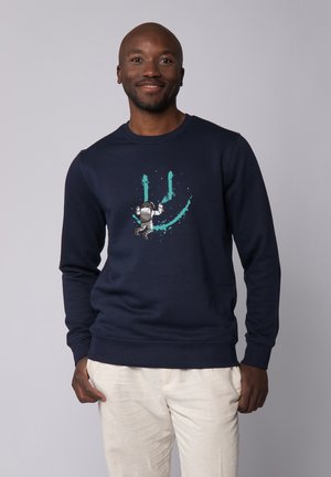 Donkerblauwe sweatshirt met een gedrukt ontwerp van een astronaut, met levendige teal accenten en spattenpatronen. Gemaakt van een katoenmix.