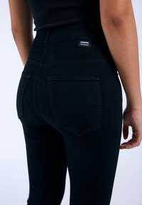 Mustat korkeavyötäröiset farkut slim fit -mallilla, joissa on takataskut ja pieni etiketti vyötärön kohdalla. Sileä kangas.