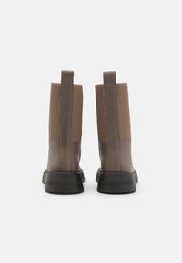 Brune lær ankelsko med ribbet beige stoffpaneler, firkantet tå og svarte gummisåler med preget merke ved hælen.