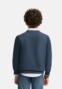Sudadera azul marino con cuello redondo, puños y dobladillo acanalados, que presenta una textura suave y un ajuste casual, llevada sobre una camisa blanca.