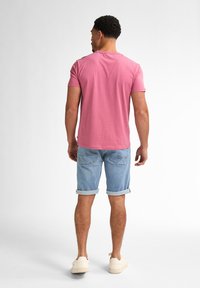 T-shirt di cotone rosa a maniche corte, abbinato a pantaloni shorts di denim azzurro chiaro. Presenta un orlo arrotolato e due tasche posteriori.