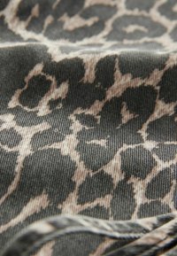 Stoff mit einem schwarz-braunen Leopardenmuster, der eine strukturierte Oberfläche und sichtbare Rippungen im Material aufweist.