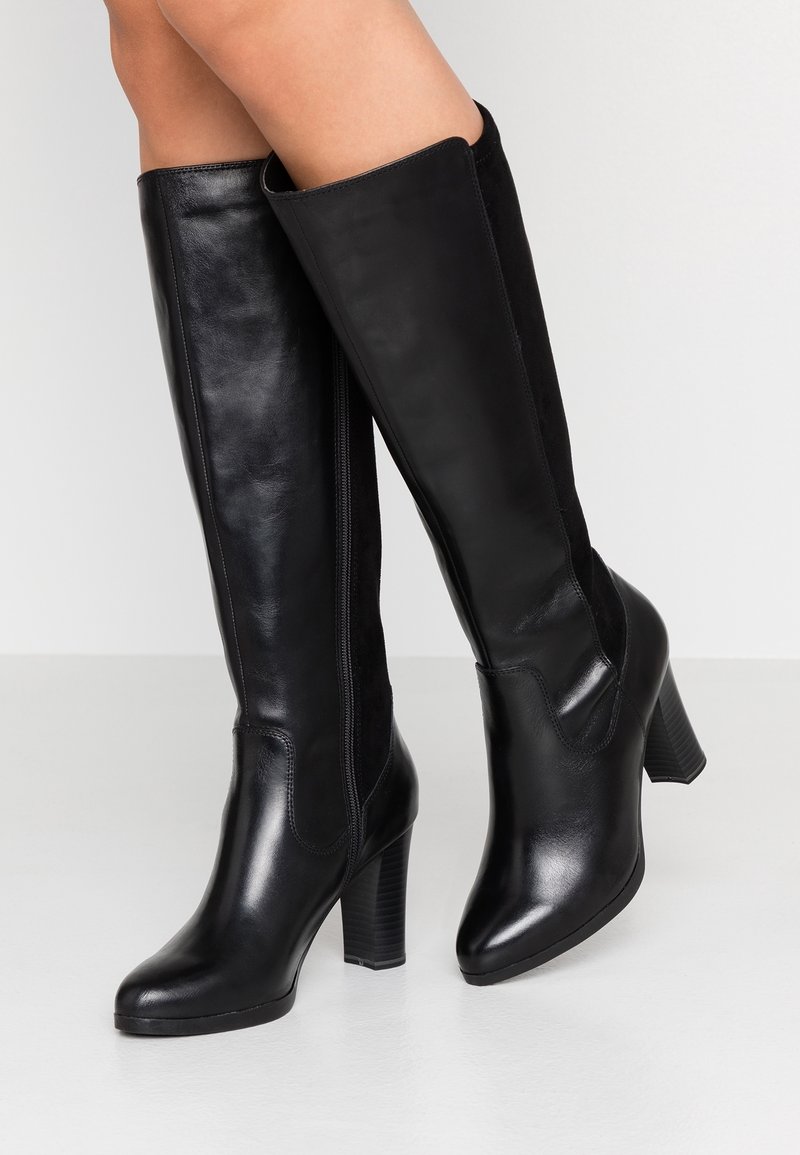 Bottes noires à hauteur de genoux avec un mélange de cuir lisse et de daim, bout pointu et talon épais avec des détails striés.