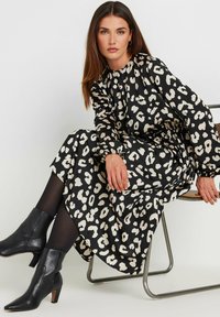 Vestido de estampado de leopardo en negro y crema con mangas largas, escote fruncido y corte relajado, combinado con botines negros.