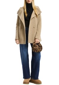 Beige tekstuuriga mantel suurte kraedega ja topelt nuppe, kombineeritud tumeda kõrge kaelusega, laia jalgadega siniste teksade ja leopardimustriga käekotiga.