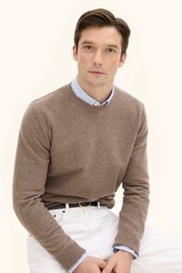 Ruskea villaneule pyöreällä kauluksella ja ribatulla vartalolla, kerroksittain vaaleansinisellä kauluspaitalla, yhdistettynä valkoisiin housuihin ja mustaan vyöhön.