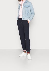 Chaqueta de mezclilla azul claro sobre una sudadera rosa con cremallera, combinada con joggers marinos con puños a rayas, complementada con zapatillas blancas.