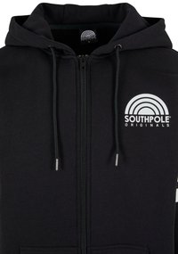 Crna zip-up dukserica izrađena od mekanog materijala, s prednjim logotipom i vezicama. Model s kapuljačom s prednjim džepovima i glatkom teksturom.