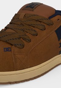 Baskets en daim marron avec des lacets marron foncé à motifs, semelle crème et détails du logo bleu foncé sur le côté et la languette.