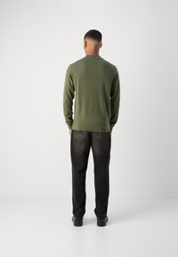 Pulover verde din tricot cu mâneci lungi, guler rotund și mansete cu model côtelé, purtat cu blugi negri din denim și încălțări negre. Văzut din spate.