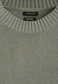 Pull vert clair en tricot à col rond avec col côtelé et deux étiquettes noires cousues à l'intérieur de l'encolure.