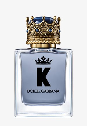 Flacon de parfum en verre transparent avec liquide bleu clair, lettre noire K, logo Dolce & Gabbana, surmonté d'un bouchon couronne doré orné.