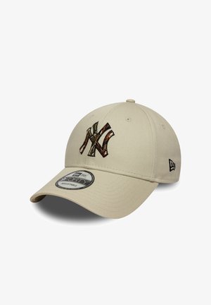 Gorra de béisbol beige con ajuste ajustable. Presenta un logo NY bordado en camuflaje y una pegatina redonda de New Era en la visera. Textura de tela suave.