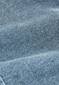 Tissu en denim bleu clair, présentant une texture lisse avec un motif en twill subtil, plié pour un effet superposé.
