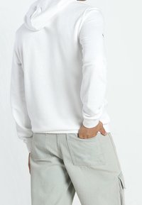 Felpa bianca con una vestibilità comoda, tasca a marsupio e polsini a coste, abbinata a pantaloni grigi chiari con più tasche.