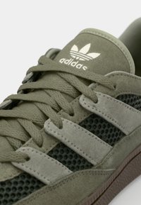 Zöld velúr és hálós sneaker három szürke csíkkal, texturált felsőrész és barna gumitalp jellemzi, az adidas logo a nyelvén található.
