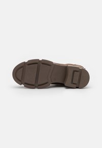 Semelle de chaussure en caoutchouc brun avec des motifs texturés et des sections de grip définies. Présente un bout arrondi et un talon plat pour plus de stabilité.